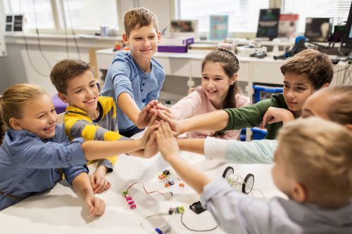 education, children, technology, science and people concept - group of happy kids building robots and making high five gesture at robotics school